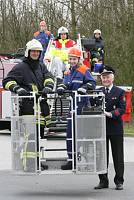 Mehrere Feuerwehrleute in Schutzkleidung stehen vor einem Feuerwehrfahrzeug mit Hubrettungskorb. Ein Feuerwehrmann in uniformierter Leitung hält den Korb fest, während die Kolleg:innen darin stehen. Im Hintergrund sieht man weitere Feuerwehrleute auf dem Fahrzeug. Die Szene vermittelt den Fokus auf Arbeitssicherheit und Teamarbeit bei der Feuerwehr, passend zur Prävention im Arbeitsschutz.
