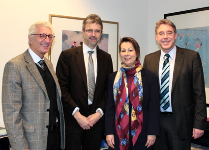 Vier Personen in formeller Kleidung lächeln in die Kamera.