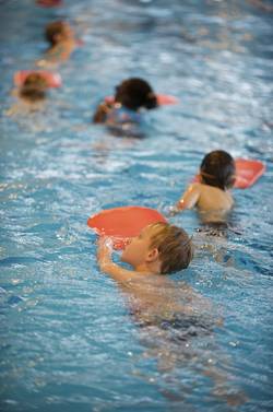 Kinder schwimmen mit Schwimmbrettern im Schwimmbecken.