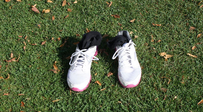 Weiße Sportschuhe mit rosa Details auf grasbewachsenem Boden.