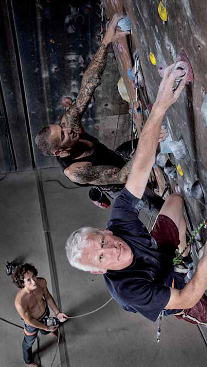 Das Bild zeigt einen jüngeren und einen älteren Mann an einer Kletterwand. Sie werden von einem dritten Mann am Boden gesichert.