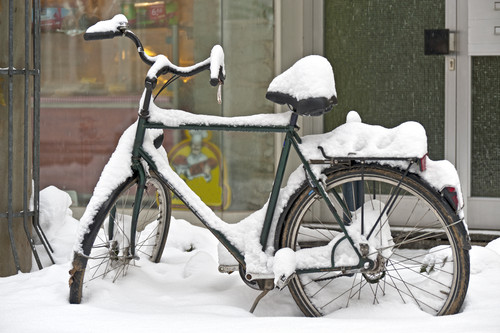 Ein altes Fahrrad, bedeckt mit Schnee, steht vor einem Gebäude. Der Schnee könnte ein Risiko für Rutschen oder andere Unfälle darstellen. Im Hintergrund ist ein Schaufenster zu sehen. Diese Szene betont die Bedeutung von sicherem Abstellen von Fahrrädern im Winter und der Prävention von Arbeitsunfällen aufgrund von winterlichen Witterungsbedingungen.