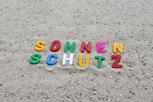 Das Bild zeigt das Wort Sonnenschutz in bunten Buchstaben an einem Strand