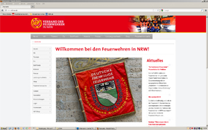 Screenshot einer Webseite des Feuerwehrverbands Nordrhein-Westfalen. Oben ein rotes Banner mit dem Logo und Schriftzug des Verbands. Darunter ein großes Begrüßungsbanner mit der Aufschrift 'Willkommen bei den Feuerwehren in NRW!' Links eine Navigationsleiste und rechts aktuelle Nachrichten. Im Zentrum ein Bild einer Fahne der Deutschen Freiwilligen Feuerwehr mit Wappen.