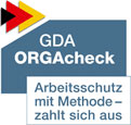 Das Bild zeigt das GDA ORGAcheck Logo. Oben links befinden sich Pfeile in den Farben Schwarz, Rot und Gelb. Daneben steht 'GDA ORGAcheck'. Darunter ist ein Slogan in blauer Schrift: 'Arbeitsschutz mit Methode – zahlt sich aus'. Das Logo steht in Zusammenhang mit Arbeitsschutzmaßnahmen und Präventionsstrategien, relevant für die Unfallkasse NRW.