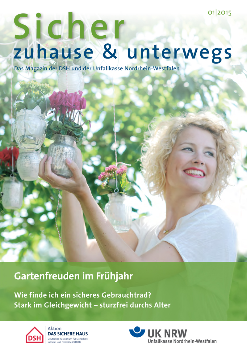 Titelbild des Magazins 'Sicher zuhause & unterwegs' von Januar 2015. Eine Frau hängt weiße Laternen im Garten auf. Im Hintergrund sind blühende Pflanzen zu sehen. Der Fokus liegt auf dem Thema 'Gartenfreuden im Frühjahr'. Das Magazin ist eine Veröffentlichung der DSH und Unfallkasse NRW mit Schwerpunkten auf Arbeitsschutz und Prävention.