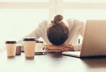 Person liegt erschöpft am Schreibtisch neben Laptop.