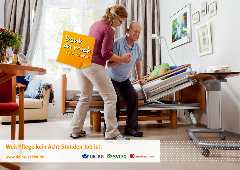 In einem hellen Zimmer hilft eine Pflegekraft einem älteren Mann, der auf einem verstellbaren Pflegebett sitzt, beim Aufstehen. Die Pflegekraft nutzt einen Transfergürtel zur Unterstützung. Im Hintergrund sind ein Fenster mit weißen Vorhängen, ein Bild an der Wand und verschiedene Möbelstücke zu sehen. Eine orangefarbene Sprechblase mit der Aufschrift 'Denk an mich. Dein Rücken' schwebt über der Szene. Unten im Bild sind Logos von UK BG, SVLFG und Knappschaft sowie der Slogan 'Weil Pflege kein Acht-Stunden-Job ist' zu sehen, mit der Website www.deinruecken.de.