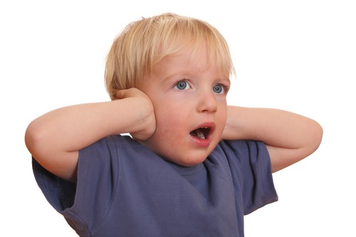 Junger blonder Junge in einem blauen T-Shirt hält sich mit beiden Händen die Ohren zu. Der Gesichtsausdruck des Kindes wirkt überrascht oder erschrocken. Das Bild kann im Kontext von Arbeitsschutzmaßnahmen oder Lärmprävention verwendet werden, um auf den Schutz vor Lärmbelästigung aufmerksam zu machen.