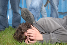 Person am Boden, Fuß steht auf Kopf, umstehende Menschen.