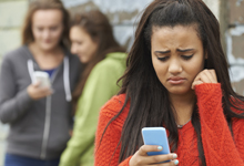 Frau schaut besorgt auf ihr Handy, zwei Personen im Hintergrund.