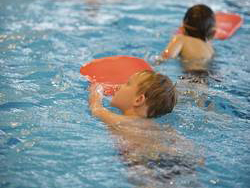 Zwei Kinder schwimmen in einem Pool und halten rote Schwimmbretter. Sie sind in flachem Wasser, konzentriert bei der Übung. Diese Aktivität fällt unter Maßnahmen zur Unfallverhütung im Kontext von Wasseraktivitäten und zur Förderung der Sicherheit im Wasser für Kinder. Die Unfallkasse NRW könnte solche Programme unterstützen, um das Bewusstsein für sichere Schwimmpraktiken zu stärken.