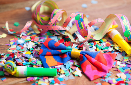 Das Bild zeigt eine fröhliche Partydekoration mit buntem Konfetti, Papierschlangen und einer farbenfrohen Schleife auf einem Holztisch. Diese lebendige Darstellung symbolisiert Feierlichkeiten. Im Kontext der Unfallkasse NRW könnte es Hinweise auf die Wichtigkeit von Arbeitsschutz und Sicherheitsmaßnahmen in entspannter Umgebung geben, um Unfälle und Verletzungen zu vermeiden.