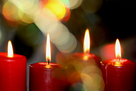 Vier brennende rote Kerzen mit unscharfen Weihnachtslichtern.