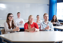 Eine Gruppe von sechs jungen Erwachsenen sitzt an Tischen in einem hellen Schulungsraum. Im Hintergrund ist eine weiße Tafel sichtbar. Die Personen wirken aufmerksam und interessiert und tragen unterschiedliche, legere Kleidung. Dies könnte eine Schulung oder ein Vortrag im Rahmen der Unfallkasse NRW zur Förderung von Arbeitsschutz und Prävention darstellen.