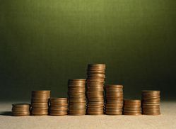 Das Bild zeigt acht unterschiedlich hohe Stapel aus Münzen, die auf einer ebenen Fläche vor einem grünen Hintergrund angeordnet sind. Die Münzen symbolisieren ökonomische Aspekte, die im Kontext des Arbeitsschutzes und der Prävention zur Vermeidung von Kosten durch Arbeitsunfälle oder Gesundheitsrisiken relevant sind. Das Bild vermittelt die Bedeutung von finanzieller Vorsorge und Investitionen in Sicherheitsmaßnahmen am Arbeitsplatz.