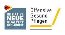 Das Bild zeigt das Logo der Initiative Neue Qualität der Arbeit (INQA) mit einem stilisierten Pfeil in den deutschen Nationalfarben und den Schriftzügen 'INITIATIVE NEUE QUALITÄT DER ARBEIT' sowie 'Offensive Gesund Pflegen', ergänzt durch ein stilisiertes gelbes Pflegebett. Das Logo reflektiert die Themen Arbeitsschutz und Prävention für bessere Arbeitsbedingungen im Pflegebereich, relevant im Kontext der Unfallkasse NRW.