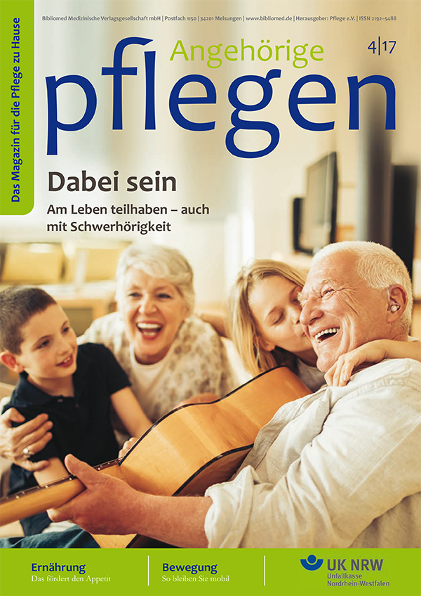 Familie sitzt lachend auf dem Sofa, Großvater spielt Gitarre.