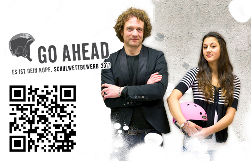 Ein Mann in einem schwarzen Anzug steht mit verschränkten Armen neben einer Frau, die einen pinken Fahrradhelm hält. Sie stehen vor einer grauen Wand mit dem Schriftzug 'GO AHEAD - Es ist dein Kopf. Schulwettbewerb 2017'. Links ist ein QR-Code abgebildet. Thema ist Arbeitsschutz und Prävention, relevant für die Unfallkasse NRW.