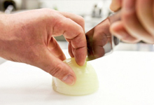 Hände schneiden eine Zwiebel mit einem Messer.