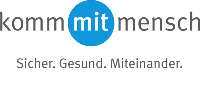 Das Bild zeigt das Logo der Präventionskampagne 'komm mit mensch' der Unfallkasse NRW. Im Zentrum steht ein blauer Kreis mit dem Wort 'mit'. Links und rechts davon die Wörter 'komm' und 'mensch', zusammen der Schriftzug 'komm mit mensch'. Darunter der Slogan 'Sicher. Gesund. Miteinander.'. Die Kampagne zielt darauf ab, Sicherheit und Gesundheit am Arbeitsplatz zu fördern.