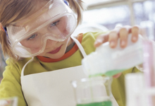 Kind im Labor gießt grüne Flüssigkeit.