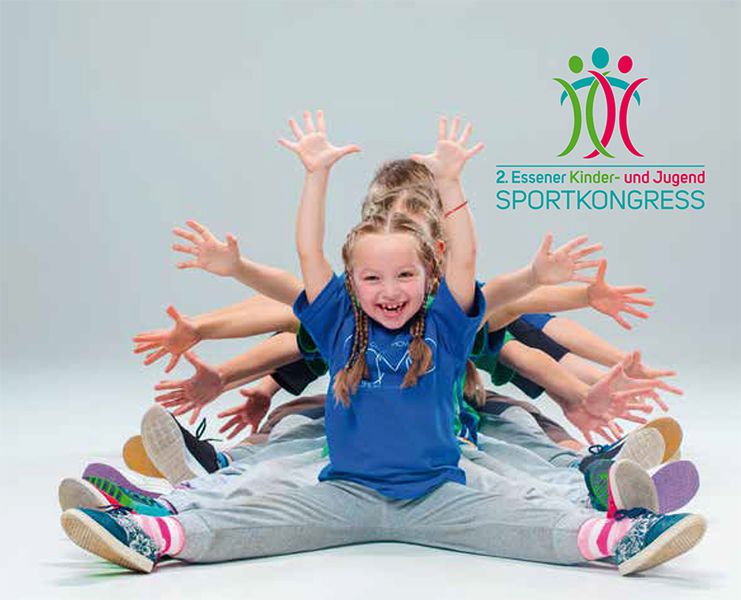Eine Gruppe von Kindern in sportlicher Kleidung sitzt auf dem Boden und macht eine Dehnübung. Alle strecken die Beine nach vorne und heben die Arme in die Luft. Im Hintergrund ist das Logo des 2. Essener Kinder- und Jugendsportkongresses zu sehen. Der Kontext legt einen Fokus auf die Bedeutung von Bewegung und Prävention im Bereich Sicherheit und Gesundheit von Kindern im Sport.