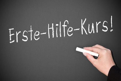 Ein Hand schreibt 'Erste-Hilfe-Kurs!' auf eine Tafel.