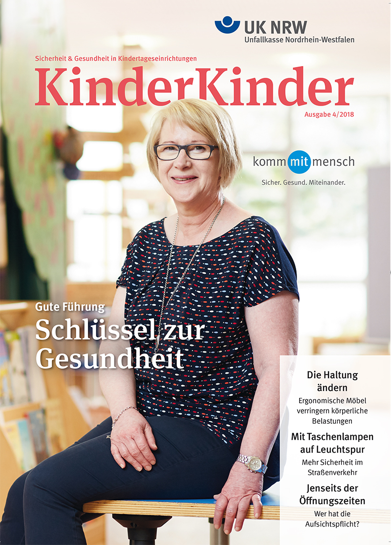 Das Titelblatt der Zeitschrift KinderKinder der Unfallkasse Nordrhein-Westfalen, Ausgabe 4/2018. Eine Frau mittleren Alters sitzt entspannt auf einem Tisch und lächelt. Sie trägt ein blau gemustertes Oberteil und eine beige Hose. Im Hintergrund sind bunte Stühle und ein Fenster zu sehen. Oben steht: 'Sicherheit & Gesundheit in Kindertageseinrichtungen. UK NRW Unfallkasse Nordrhein-Westfalen.' Der Titelartikel lautet: 'Gute Führung - Schlüssel zur Gesundheit'. Weitere Artikel auf der Titelseite beschäftigen sich mit der Haltung, ergonomischen Möbeln, Taschenlampen mit Leuchtspur im Straßenverkehr und den Öffnungszeiten von Kitas.