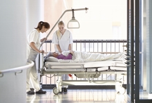 Pflegekräfte schieben Patientenbett auf Krankenhausflur.