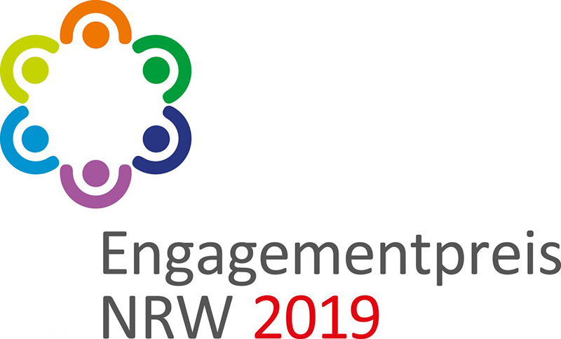 Das Logo für den Engagementpreis NRW 2019 zeigt abstrakte Figuren in einem Kreis dargestellt, jede in einer anderen Farbe (blau, grün, gelb, orange, rot, violett). Darunter steht in grau 'Engagementpreis NRW' und in rot '2019'. Das Logo symbolisiert gemeinschaftliches Engagement und Vielfalt, relevant für die Unfallkasse NRW im Kontext von Arbeitsschutz und Prävention im gesellschaftlichen Engagement.
