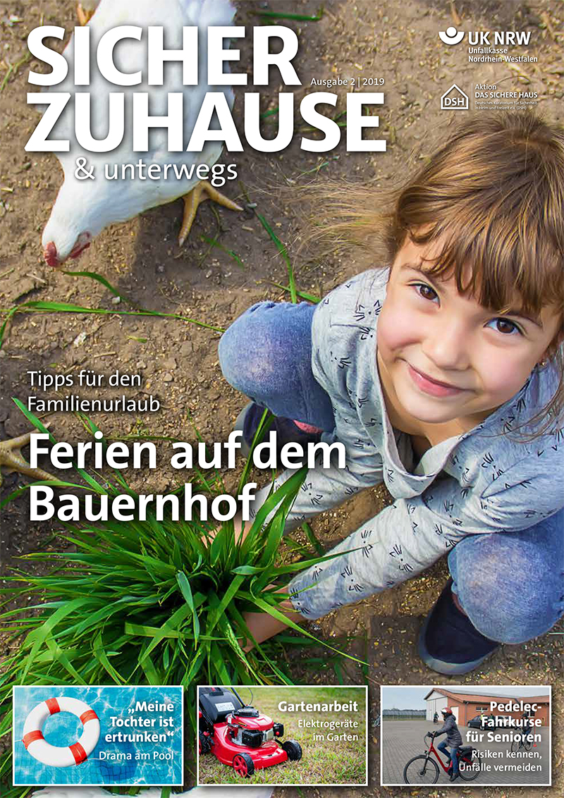 Ein lächelndes Mädchen kniet auf einem Bauernhof und streckt die Hand zu einem weiß-braunen Huhn aus, das interessiert pickt. Im Hintergrund sind Gras und ein Eimer zu sehen. Der Name der Zeitschrift ist 'Sicher Zuhause & Unterwegs', herausgegeben von der Unfallkasse NRW. Auf dem Cover sind zusätzlich Themen wie Tipps für den Familienurlaub, Elektrogeräte Sicherheit beim Gärtnern und Prävention von Unfällen älterer Menschen aufgeführt.