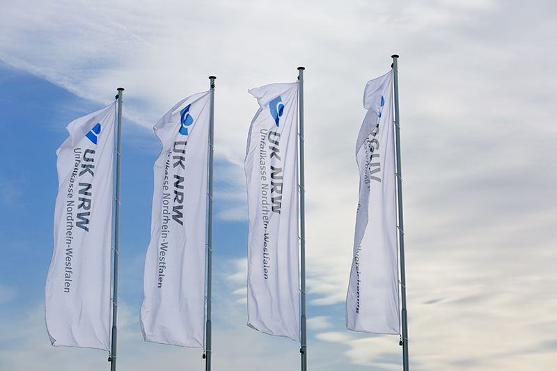 Vier Flaggen der Unfallkasse NRW wehen im Wind.