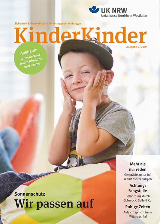 Ein Junge mit Mütze sitzt in einer Kindertageseinrichtung vor einem Plakat. Das Plakat ist mit Informationen zum Arbeitsschutz und Prävention durch die Unfallkasse NRW beschriftet. Es bezieht sich auf Sonnenschutz und beinhaltet Schlagworte wie 'Sonnenschutz', 'Wir passen auf', sowie Hinweise auf Kleidung und Creme. Das Cover der Ausgabe 'KinderKinder' thematisiert Arbeitsschutz und Prävention in Kindergärten.