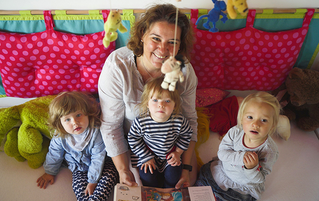 Erwachsene liest mit drei Kleinkindern ein Buch.