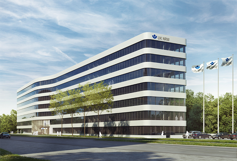 Modernes, mehrstöckiges Bürogebäude der Unfallkasse Nordrhein-Westfalen mit geschwungener Architektur. Drei Flaggen mit dem Logo der UK NRW stehen vor dem Gebäude. Die Unfallkasse ist auf Arbeitsschutz und Prävention spezialisiert. Eine ruhige Straße und Bäume umgeben das Gebäude unter einem blauen Himmel mit weißen Wolken.