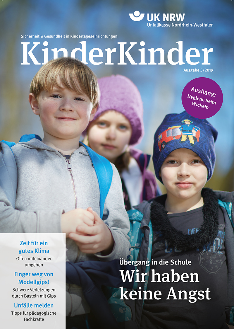 Das Cover der Zeitschrift 'KinderKinder' der Unfallkasse Nordrhein-Westfalen zeigt drei Kinder im Freien. Der Junge links trägt eine blaue Jacke und Mütze, das Mädchen rechts eine schwarz-weiße Mütze mit Blumenmuster, und der Junge in der Mitte hat eine graue Jacke und blaue Mütze. Oben steht 'Sicherheit & Gesundheit in Kindertageseinrichtungen' und 'UK NRW Unfallkasse Nordrhein-Westfalen'. Themen wie 'Übergang in die Schule - Wir haben keine Angst', 'Zeit für ein gutes Klima', 'Modellpuppe' und weitere, die sich auf Kindersicherheit und Gesundheit fokussieren, sind ebenfalls aufgelistet. Ein lila Kreis mit dem Hinweis 'Aushang: Hygiene beim Wickeln' befindet sich rechts oben.