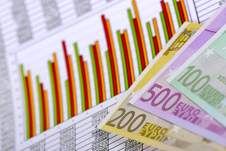 Einige Euro-Geldscheine in verschiedenen Werten liegen auf einem Dokument. Im Hintergrund sind bunte Balkendiagramme sichtbar, die auf wirtschaftliche Analysen oder Finanzstatistiken hinweisen. Diese Darstellung könnte im Kontext des Arbeitsschutzes die finanzielle Investition in Sicherheitsmaßnahmen und Prävention bei der Unfallkasse NRW visualisieren.
