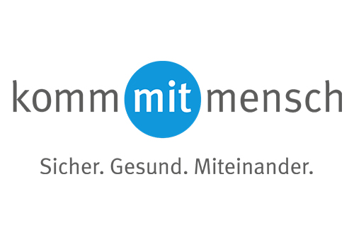 Das Bild zeigt das Logo der Kampagne 'komm mit mensch' der Unfallkasse NRW. Der Text 'komm mit mensch' ist in Grau gehalten, mit einem blauen Punkt anstelle des Wortes 'mit'. Darunter steht der Slogan: 'Sicher. Gesund. Miteinander.'. Die Kampagne fokussiert auf Arbeitsschutz und Prävention in Betrieben.
