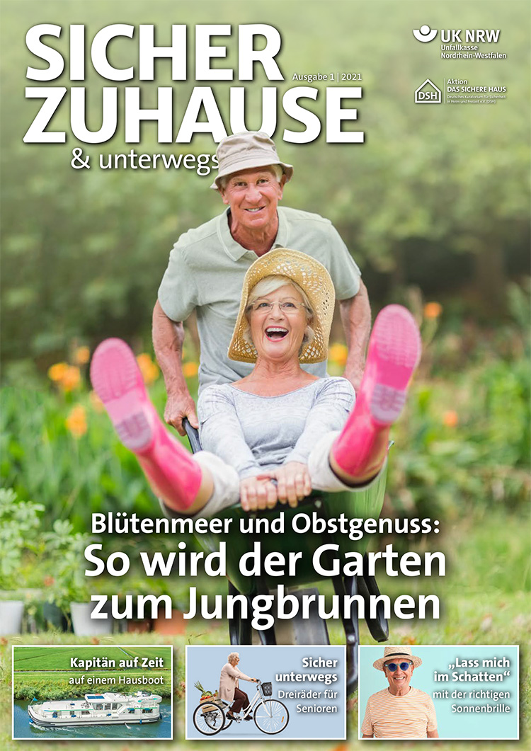 Ein älteres Paar genießt die Gartenarbeit. Die Frau sitzt lachend mit einem Strohhut auf einer Schubkarre, die von einem Mann geschoben wird. Im Hintergrund blüht ein Garten. Der Kontext des Bildes bezieht sich auf Arbeitsschutz und Prävention für ältere Personen, um sicher und gesund aktiv zu bleiben. Das Bild ist Teil eines Magazins der Unfallkasse NRW über sicheres und präventives Verhalten zu Hause und unterwegs.