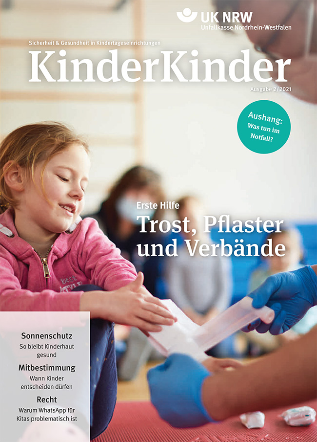 Das Cover der Zeitschrift 'KinderKinder', Ausgabe 2/2021, der Unfallkasse Nordrhein-Westfalen. Im Vordergrund ist eine Erzieherin, die einem Kind den Arm verbindet. Das Kind hält still und konzentriert den Arm ausgestreckt. Die Schlagzeile lautet 'Erste Hilfe: Trost, Pflaster und Verbände'. In einem blauen Kreis steht 'Aushang: Was tun im Notfall?'. Weitere Themen sind: Sonnenschutz für Kinder, Mitbestimmung und rechtliche Fragen zur Nutzung von WhatsApp. Der Kontext legt Fokus auf Sicherheit und Gesundheit in Kindertageseinrichtungen.