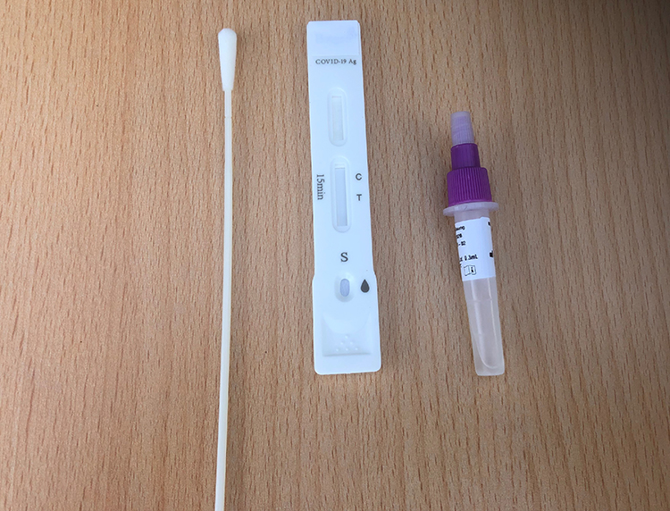 Ein COVID-19 Selbsttest-Set liegt auf einer Holzoberfläche. Es besteht aus einem Wattestäbchen zum Abstrich, einem Teststreifen mit Markierungen für Ergebnislinien und einer kleinen Flasche mit dem Tröpfchenbehälter für die Testlösung. Geeignet zur Eigenanwendung zur Identifizierung einer möglichen Infektion, relevanter Kontext für Arbeitsschutz und Prävention im Rahmen von Maßnahmen zur Eindämmung der Pandemie, relevant für Unfallkasse NRW.