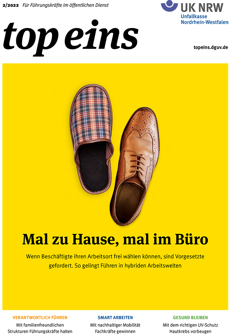 Auf einem gelben Hintergrund sind zwei verschiedene Schuhe abgebildet. Links ein lässiger, bunt karierter Hausschuh, rechts ein eleganter brauner Lederschuh. Darunter der Text: 'Mal zu Hause, mal im Büro. Wenn Beschäftigte ihren Arbeitsort frei wählen können, sind Vorgesetzte gefordert. So gelingt Führen in hybriden Arbeitswelten.' Dies illustriert das Thema flexibler Arbeitsorte und die Herausforderungen für Führungskräfte in der modernen Arbeitswelt, relevant für Arbeitsschutz und Prävention im Kontext der Unfallkasse NRW.