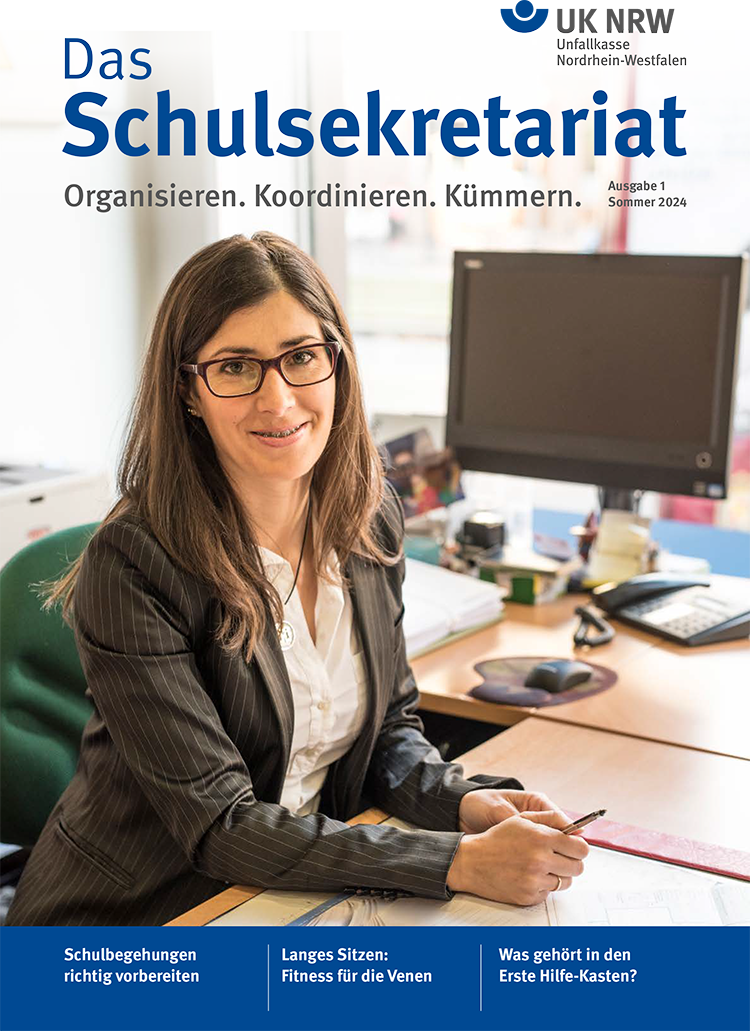Eine Frau sitzt lächelnd an einem Schreibtisch in einem Büro. Sie trägt eine Brille und formelle Kleidung. Im Hintergrund sind Büromaterialien zu sehen. Oben auf dem Bild steht der Titel 'Das Schulsekretariat' mit dem Untertitel 'Organisieren. Koordinieren. Kümmern.' sowie der Ausgabe 'Sommer 2024'. Oben rechts befindet sich das Logo der Unfallkasse Nordrhein-Westfalen. Die Themen der Ausgabe behandeln die richtige Vorbereitung von Schulbegehungen, die Bedeutung des richtigen Sitzens für die Gesundheit und den Inhalt eines Erste Hilfe-Kastens.