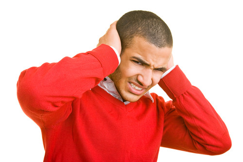 Mann in rotem Pullover hält Ohren zu und schaut angestrengt.